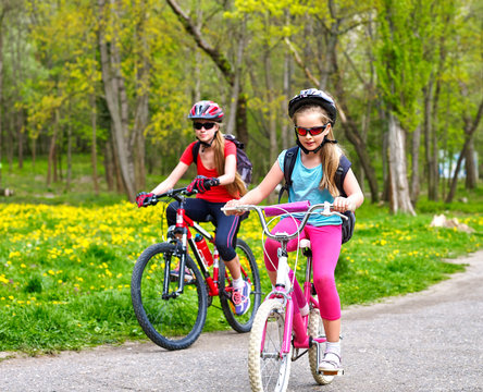 Bikes bicyclist girl. Girls wearing bicycle helmet  with rucksack ciclyng bicycle. Children outrace one another . Bike share program save money and time. Child in foreground  teenager on background.