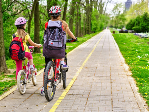 Bikes bicyclist girl. Girls wearing bicycle helmet  with rucksack ciclyng bicycle. Girls children cycling on yellow bike lane. Bike share program save money and time. Back view.
