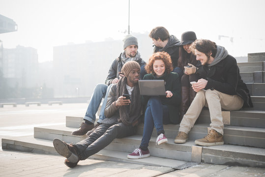 Six young adult friends on steps browsing laptop