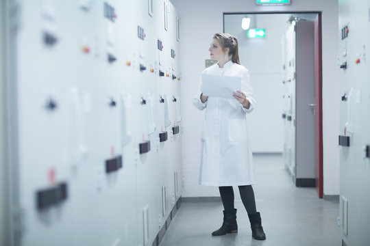 Young female scientist holding paperwork monitoring machine in technical room