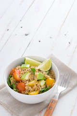 Quinoa salad in bowl, tomatoes and spinach on white wooden table
