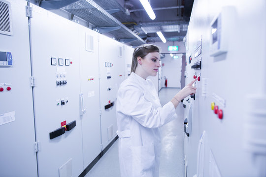 Female scientist pressing button on machine control panel in technical room