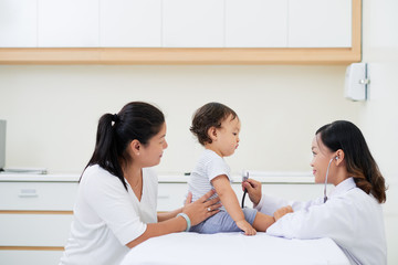 Young female pediatrician checking heartbeat of little baby