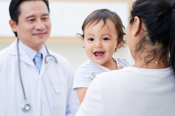 Fototapeta premium Cute baby boy laughing when his mother talking to doctor