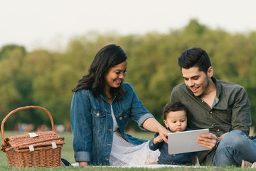 Mother, father and baby boy sitting outdoors using digital tablet