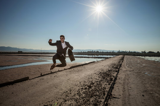 Mid adult businessman carrying briefcase jumping mid air at beach