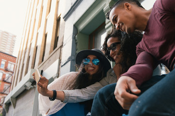 Three mid adult friends posing for smartphone selfie on city street