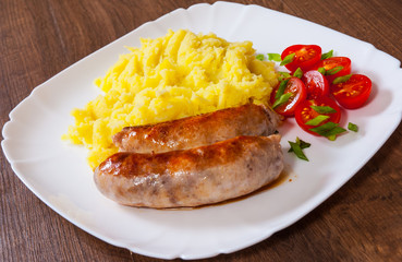 fried meat sausages with mashed potatoes and vegetables salad in a plate on wooden table