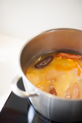 big silver metal pan with typical spanish food stew with beans native from Asturias black pudding sausage on black cooker in white kitchen
