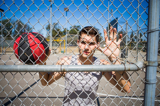 Portrait Of Young Male Basketball Player Behind Basketball Court Fence