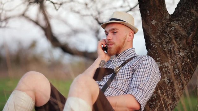 Man outdoors sitting on grass talking on a smartphone.