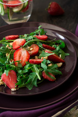 Fresh salad with strawberry, arugula and walnuts on purple plate. Low key