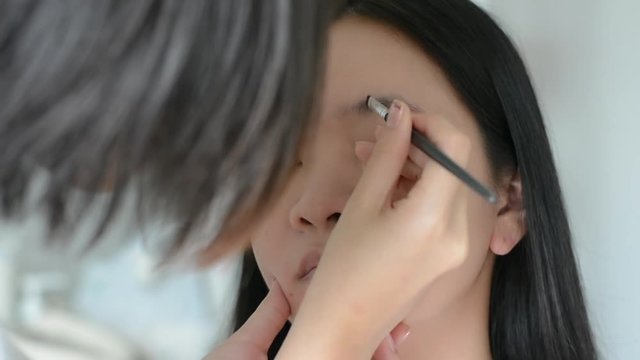 Woman is doing facial cosmetic makeup using eyebrow brush to a model in HD quality