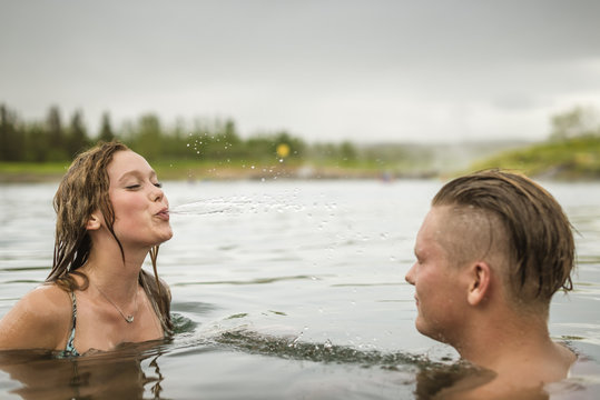 Young couple squirting water in Secret Lagoon hot spring (Gamla Laugin), Fludir, Iceland