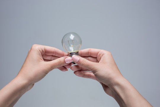 Hands holding an incandescent light bulb on gray background