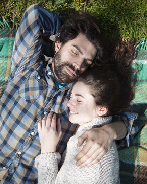 Overhead view of young couple lying with eyes closed on picnic blanket