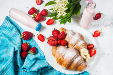 Delicious breakfast with fresh croissants and strawberries on white wooden background