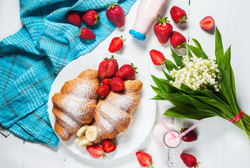 Delicious breakfast with fresh croissants and strawberries on white wooden background