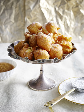 Bunuelos piled into silver serving dish dusted with icing sugar