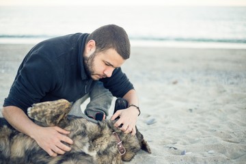 Man giving affection to the dog on a sandy beach
