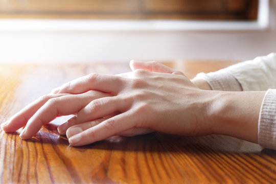 Close-up of woman hands in reflexive and concern position on wooden table