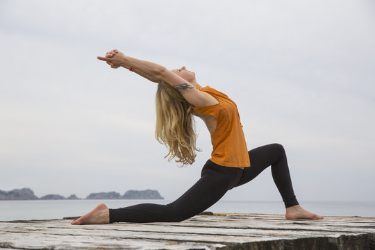 Mid adult woman bending backwards practicing yoga on wooden sea pier