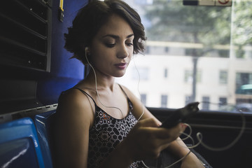 Young woman commuting on bus listening to music on smartphone, New York, US
