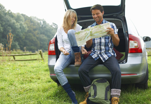 Couple at rear of car map reading preparing for walk