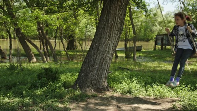 8 years old girl in plaid shirt rides a rope swing in the village in the spring in sunny weather