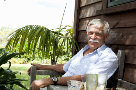 Senior man relaxing by wooden cabin, Raglan, New Zealand