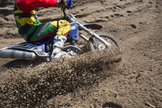 Young male motocross rider racing through mud track