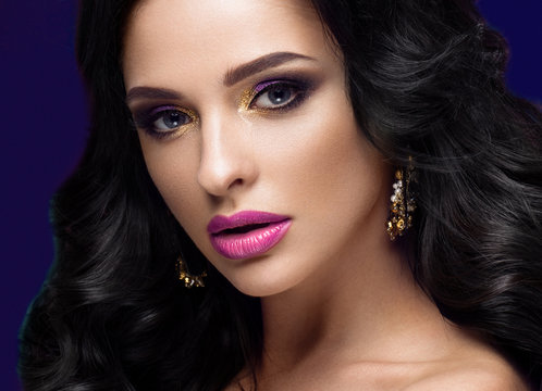 Beautiful brunette model: curls, classic makeup, gold jewelry and purple lips. The beauty face. 