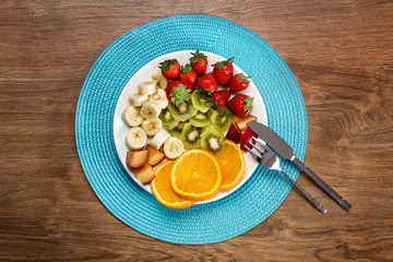 Plato de frutas variadas sobre plato blanco con cuchillo y tenedor. Vista superior