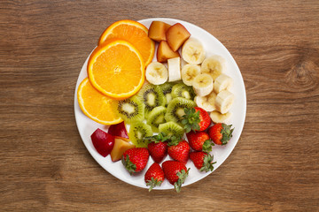 Frutas variadas sobre un plato blanco sobre un fondo de mesa de madera. Vista superior