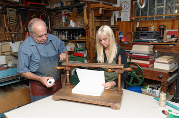 Senior man and young woman preparing to bind pages with thread in traditional bookbinding workshop