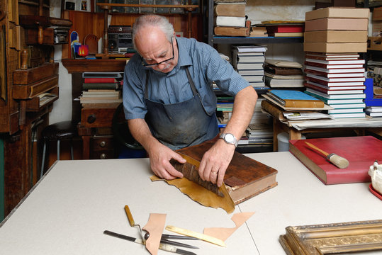 Senior man repairing antique book spine in traditional bookbinding workshop