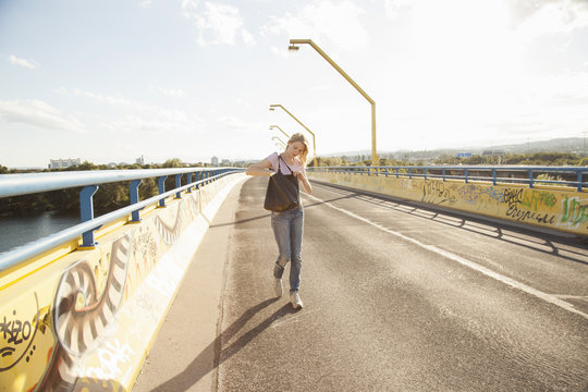 Young woman walking across bridge looking in shoulder bag