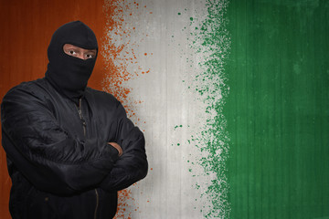 dangerous man in a mask standing near a wall with painted national flag of cote divoire