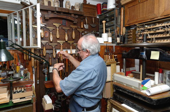 Senior man selecting tools in traditional bookbinding workshop