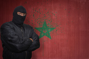 dangerous man in a mask standing near a wall with painted national flag of morocco