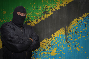 dangerous man in a mask standing near a wall with painted national flag of tanzania