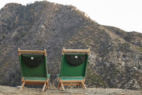 Rear view of two empty deckchairs in front of hill