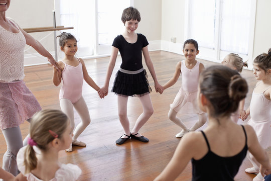 Children and teacher in circle practicing ballet in ballet school