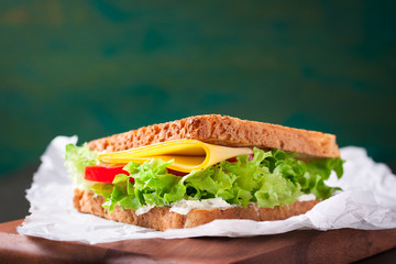 Toasted sandwich with salad leaves, tomatoes and cheese with fork on a cutting board on a green background with free space for text, closeup, horizontal.