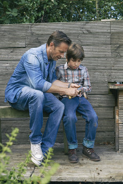 Father showing son how to use pocket knife on allotment