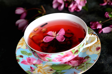 fruit tea in a cup and pink flowers on dark background