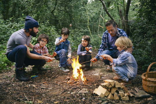 Two fathers and four boys toasting marshmallows on campfire in forest