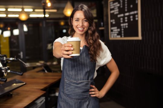 Smiling barista holding disposable cup