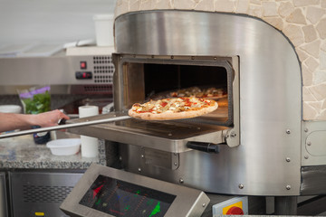 cook pulls lave baked pizzas from a stone oven