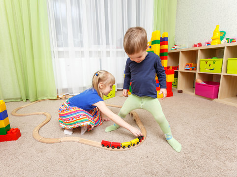 Little boy and girl play with toy railway in kindergarten